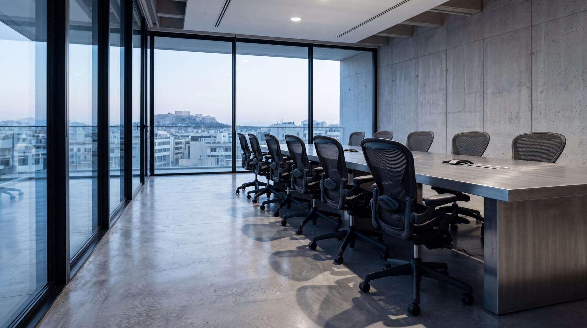 Row of empty matte-black mesh ergonomic chairs around a long brushed-steel conference table, late-afternoon light casting parallel shadows