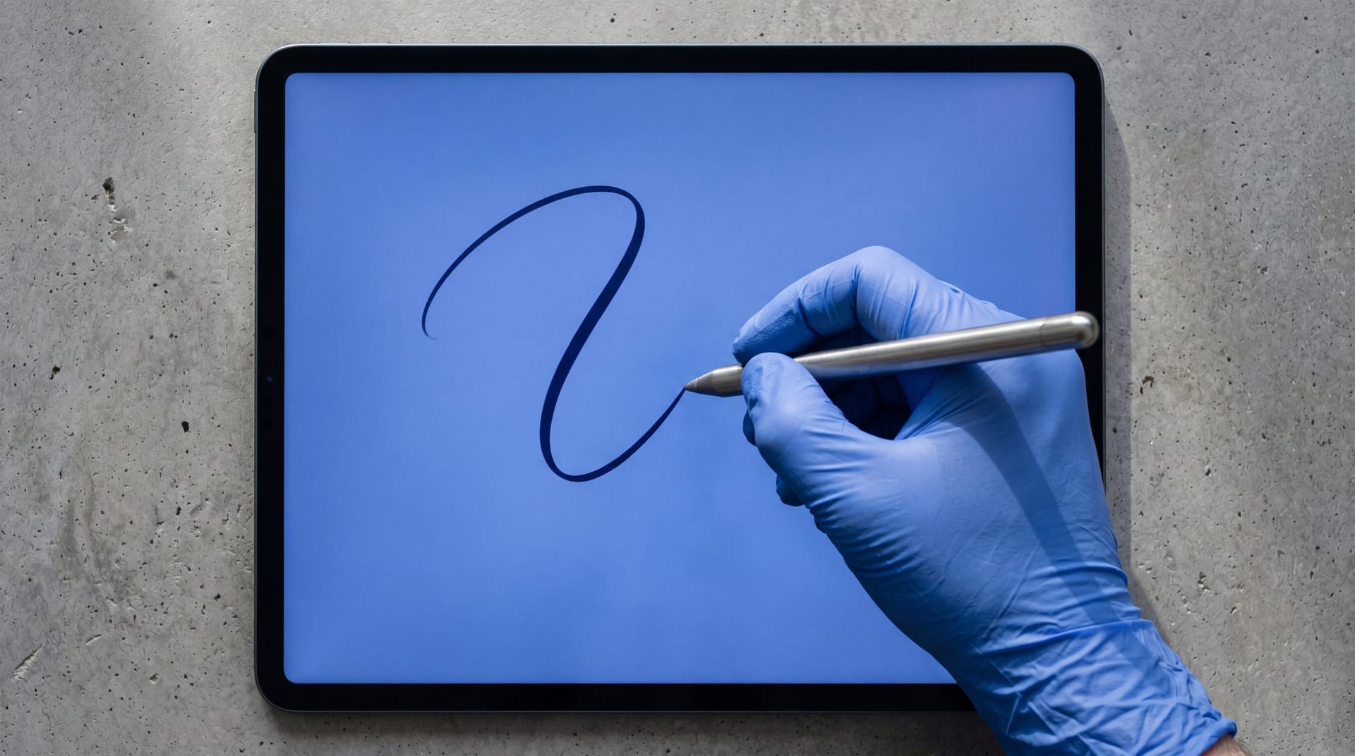 Brushed-steel stylus drawing an abstract ink curl on a tablet screen, polished concrete desk
